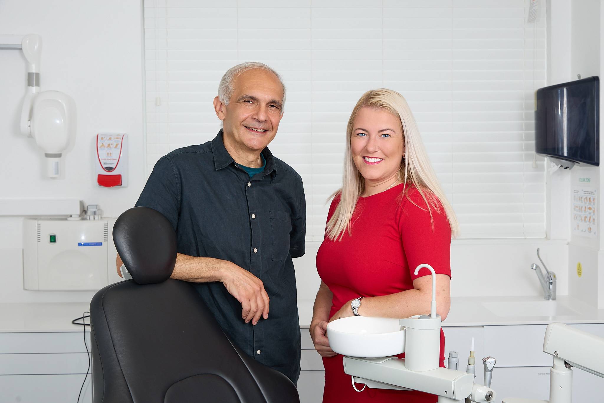Dentist Shahriar Majlessi and Practice Manager Sophie, smiling in the dental surgery whilst leaning against the chair
