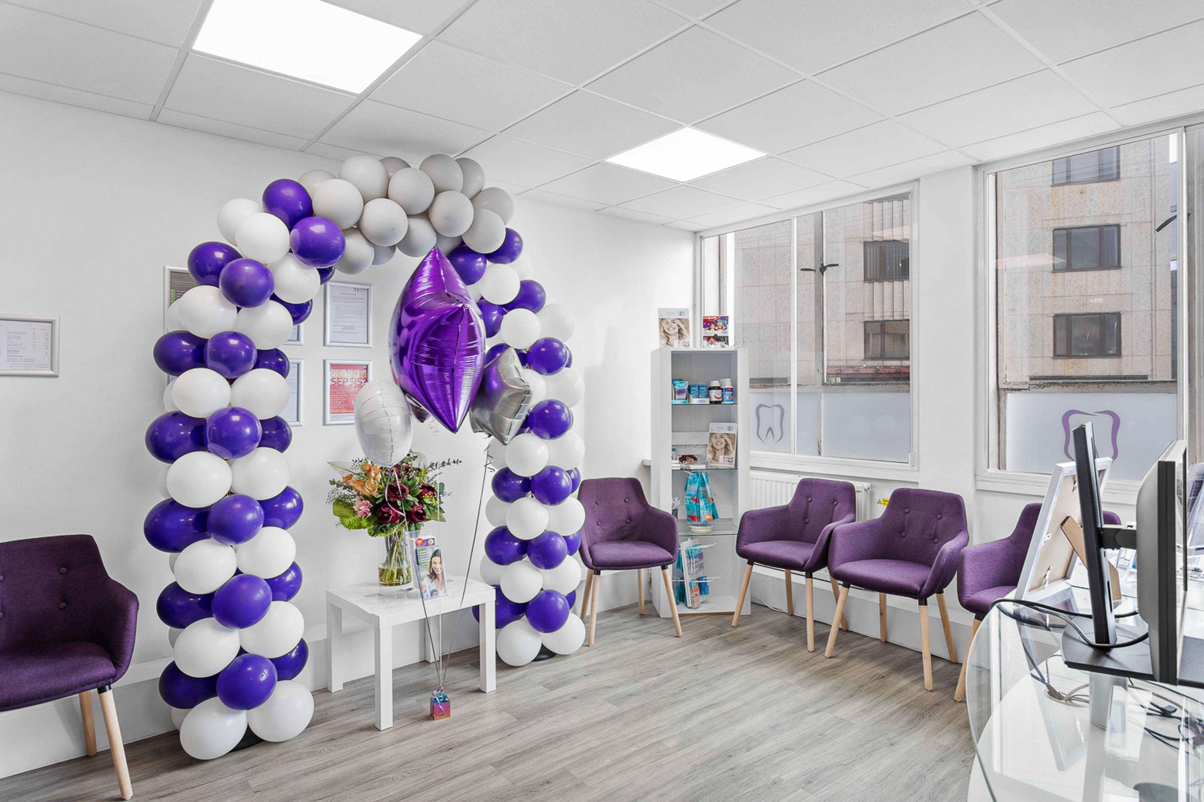 Bright and modern reception and waiting area at Plymouth City Centre Dental Practice with a purple and white balloon arch and flowers on a table