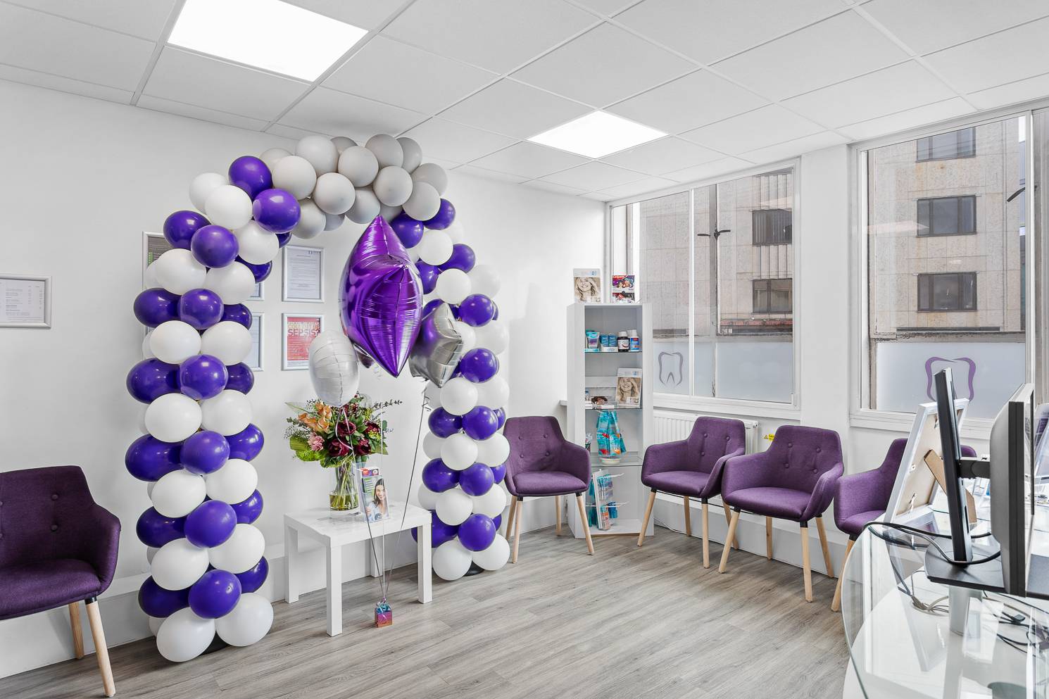 Bright and modern reception and waiting area at Plymouth City Centre Dental Practice with a purple and white balloon arch and flowers on a table