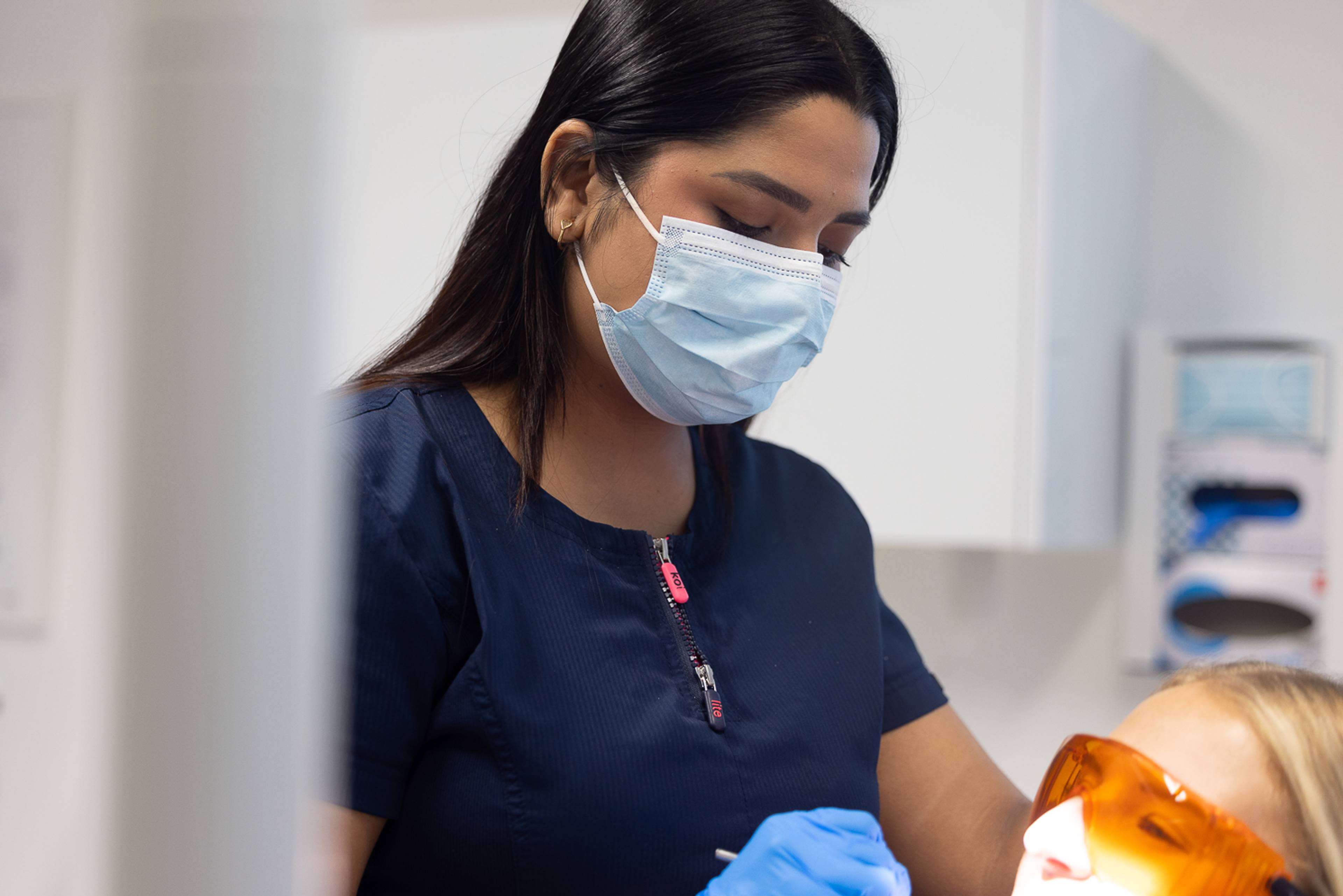 Cosmetic dentist Gayathiri Devadas examines a patient who is wearing orange eye protection goggles