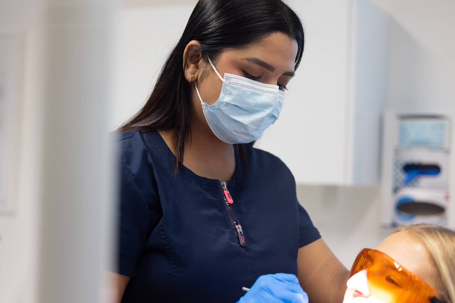 Cosmetic dentist Gayathiri Devadas examines a patient who is wearing orange eye protection goggles