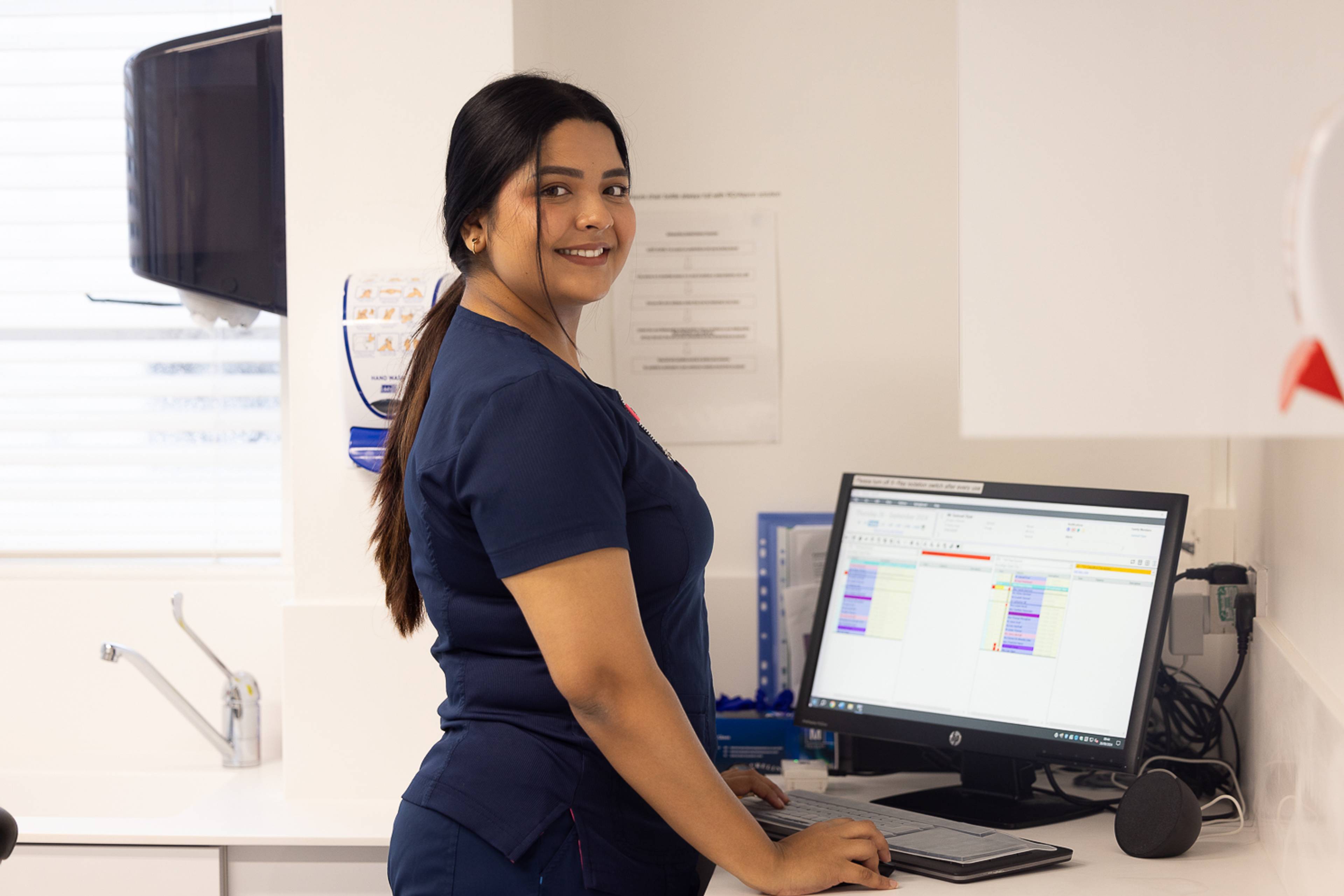 Dentist Gayathiri Devadas smiles at the camera while working at a computer screen