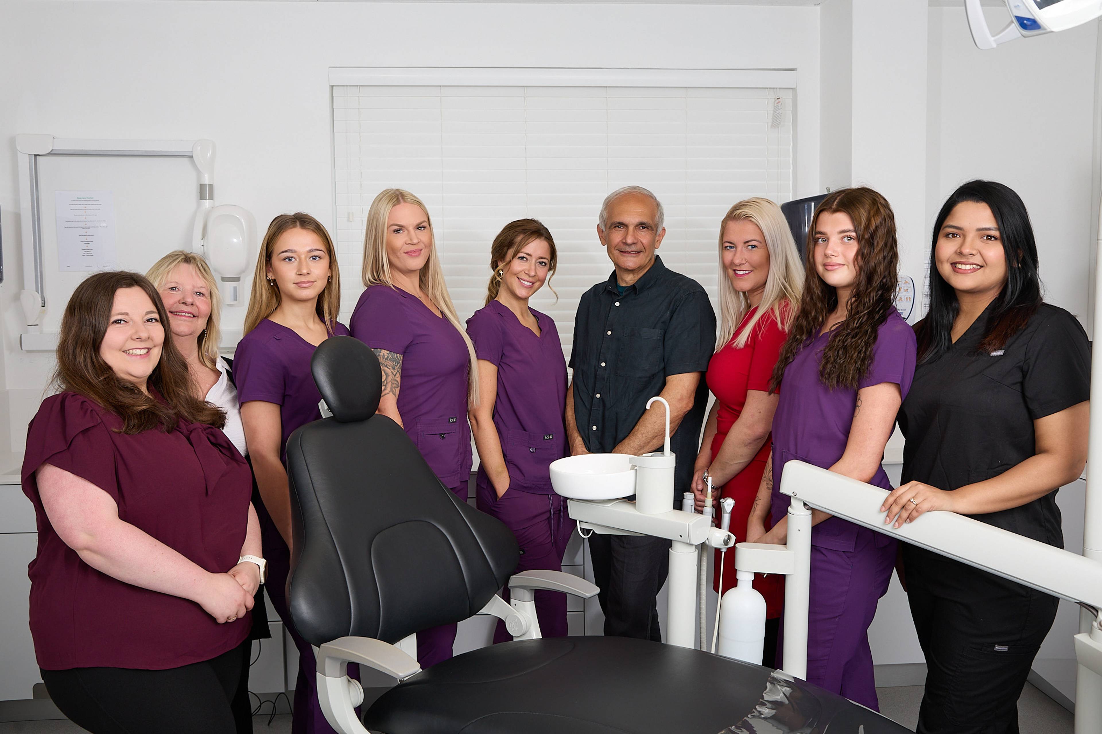 Plymouth City Centre Dental Practice team standing together smiling in a modern white surgery with a black dental chair