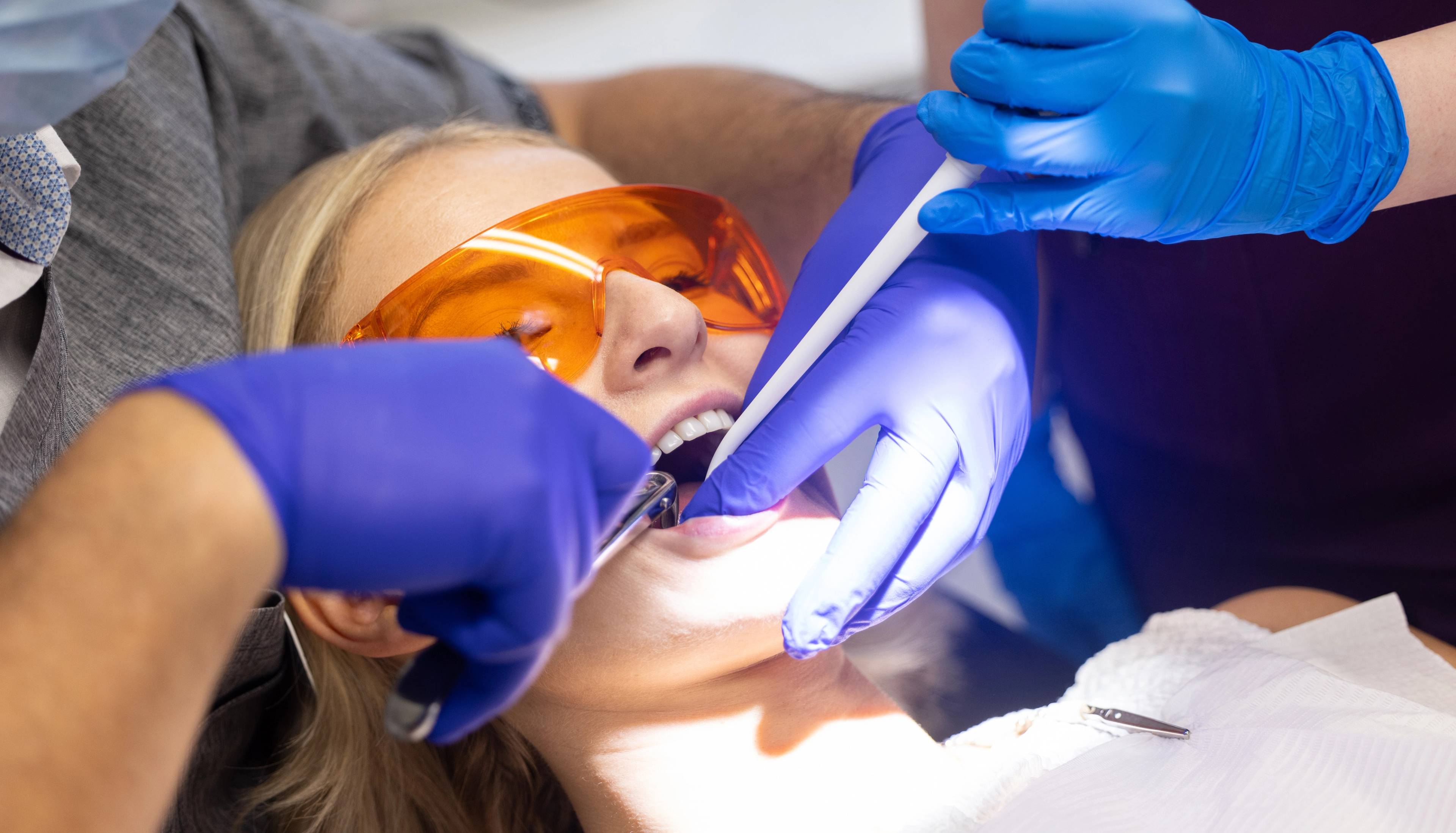 A close-up of a patient who is having her teeth examined while a dental nurse holds a suction device in the patient's mouth