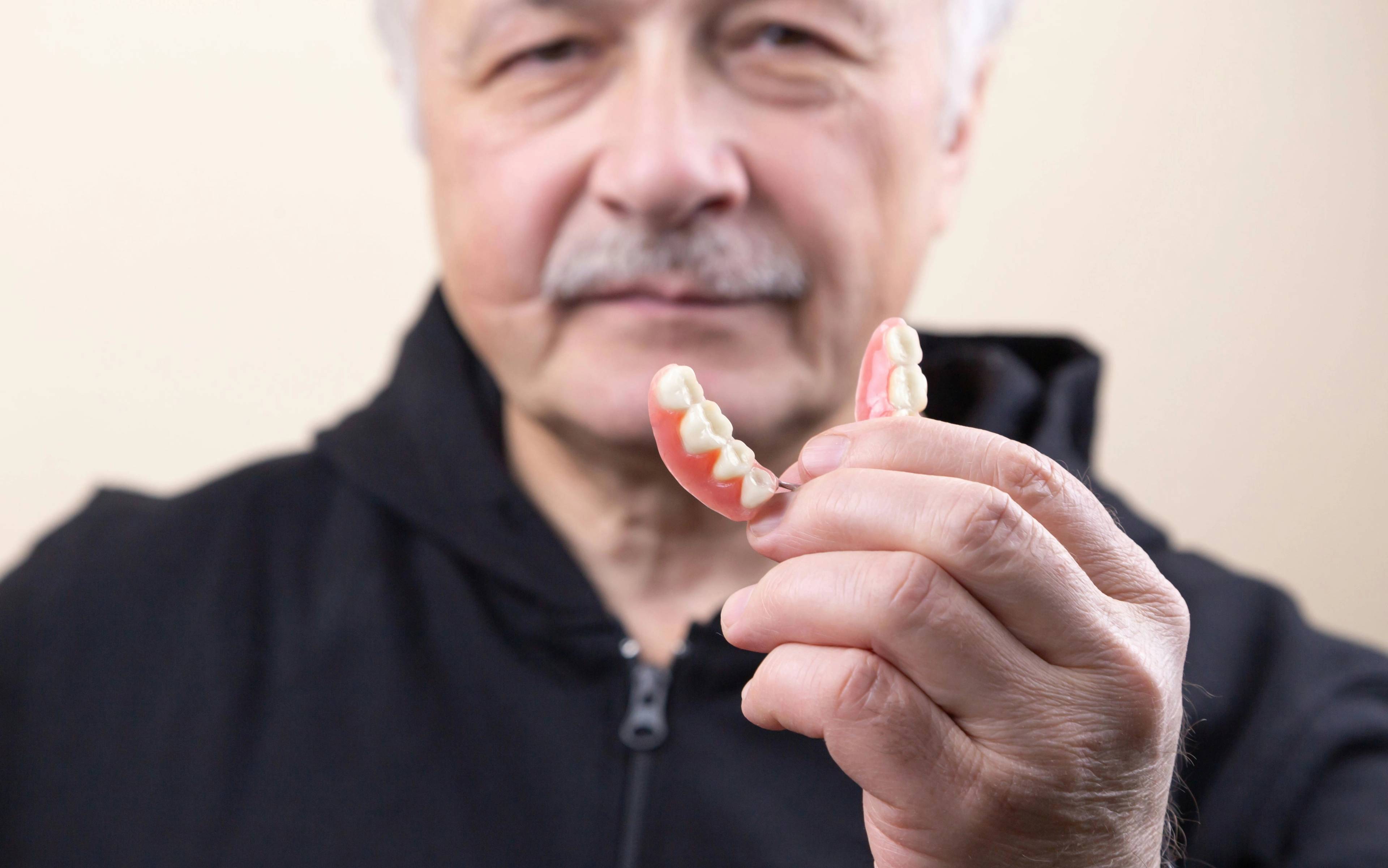 Stock photo of an older man holding partial dentures