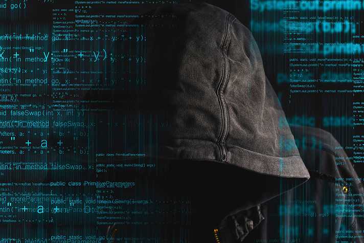 A hooded figure is seen surrounded by computer coding