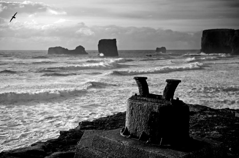 An old mooring capstan is seen beside a rocky coastline