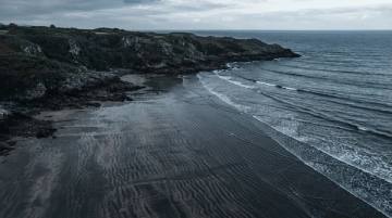 Playa de arena oscura en marea baja con las marcas del oleaje dibujando líneas paralelas