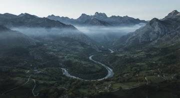Valle abriéndose entre montañas al amanecer, visto desde un dron