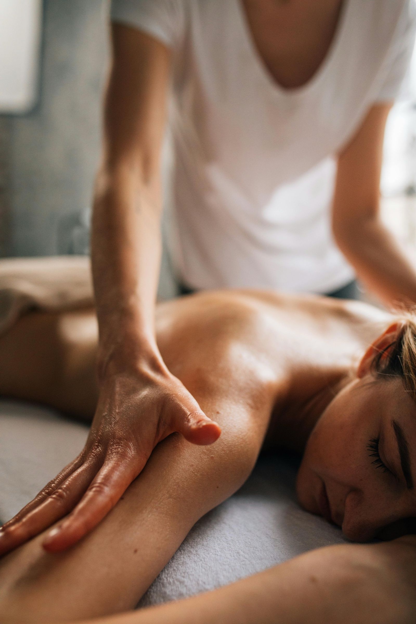 A therapist's hands working along the shoulder and back of someone lying face down on a treatment table.