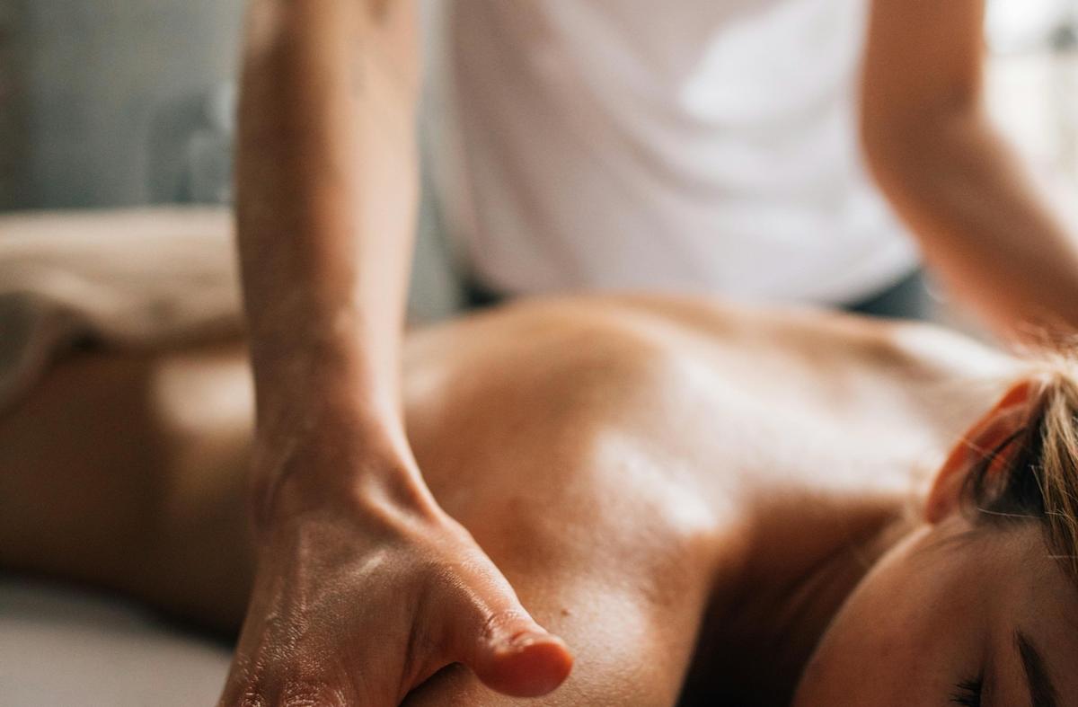 A therapist's hands working along the shoulder and back of someone lying face down on a treatment table.