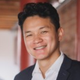 Smiling person in a dark blazer and white shirt standing indoors with a blurred background