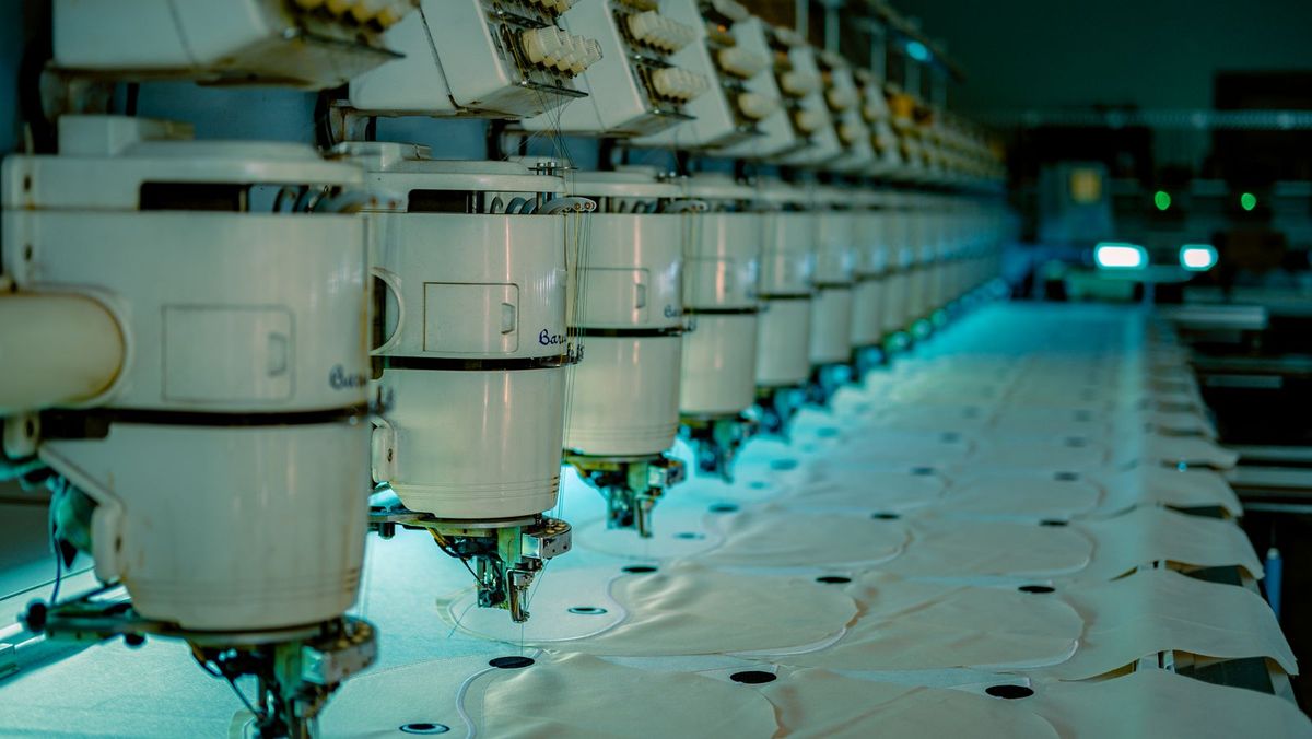 Row of industrial embroidery machines stitching patterns into white fabric.
