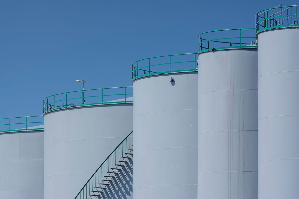 Large white industrial storage tanks with green railings and an exterior staircase under a clear blue sky.