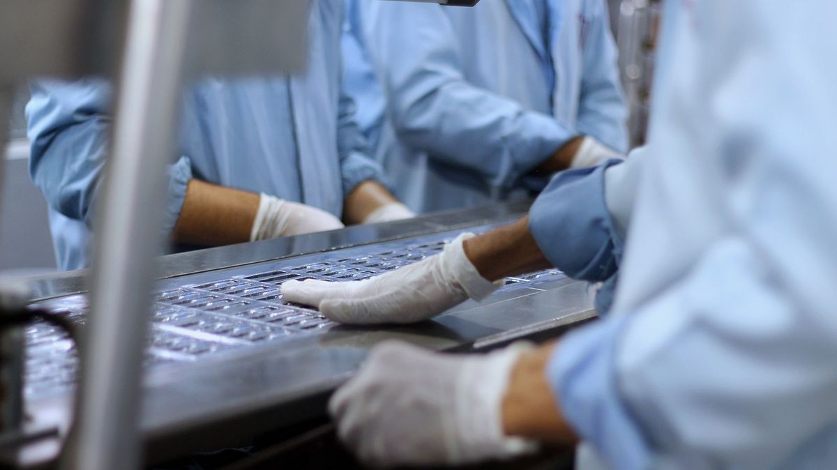 Workers in blue protective clothing and gloves handle packaged items on a production line.