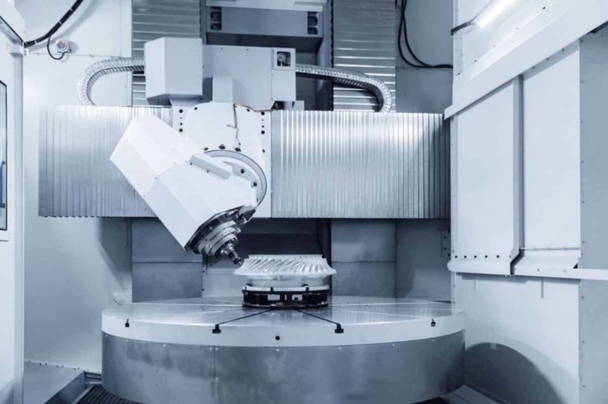 Large industrial CNC machine milling a metal turbine-like component on a circular table