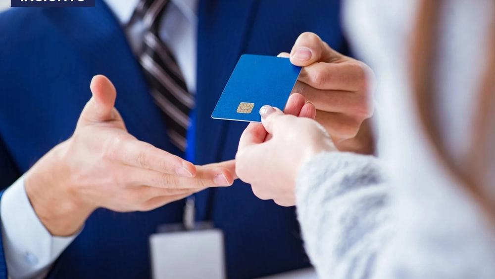 Bank employee in a blue suit hands a blue credit card to a customer