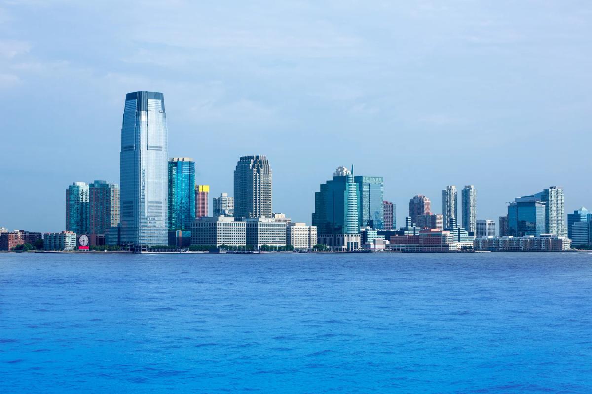 Modern city skyline with tall glass skyscrapers along a waterfront under a clear blue sky