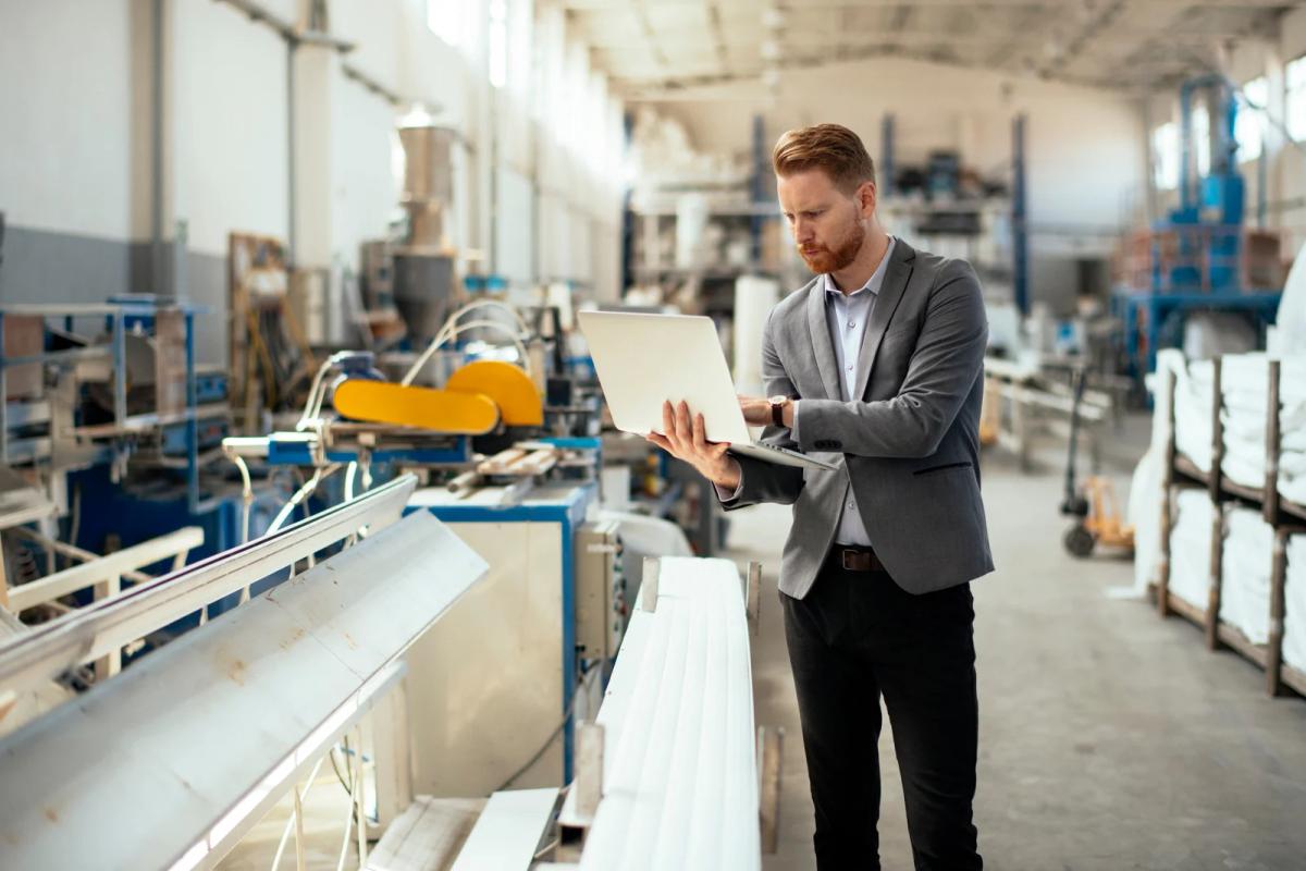 Businessman in a suit using a laptop while inspecting machinery in a bright factory