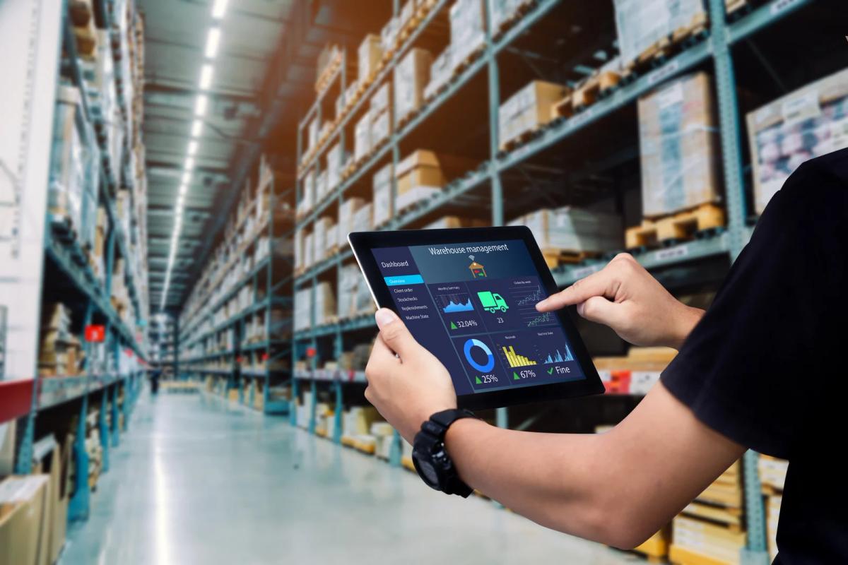 Person using a tablet with warehouse management dashboard in a large storage aisle