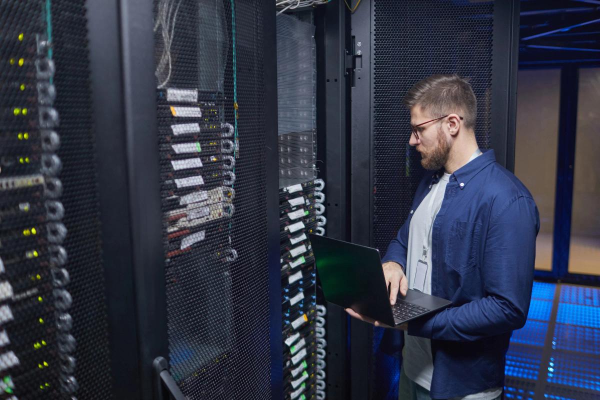 IT technician using a laptop while inspecting server racks in a data center
