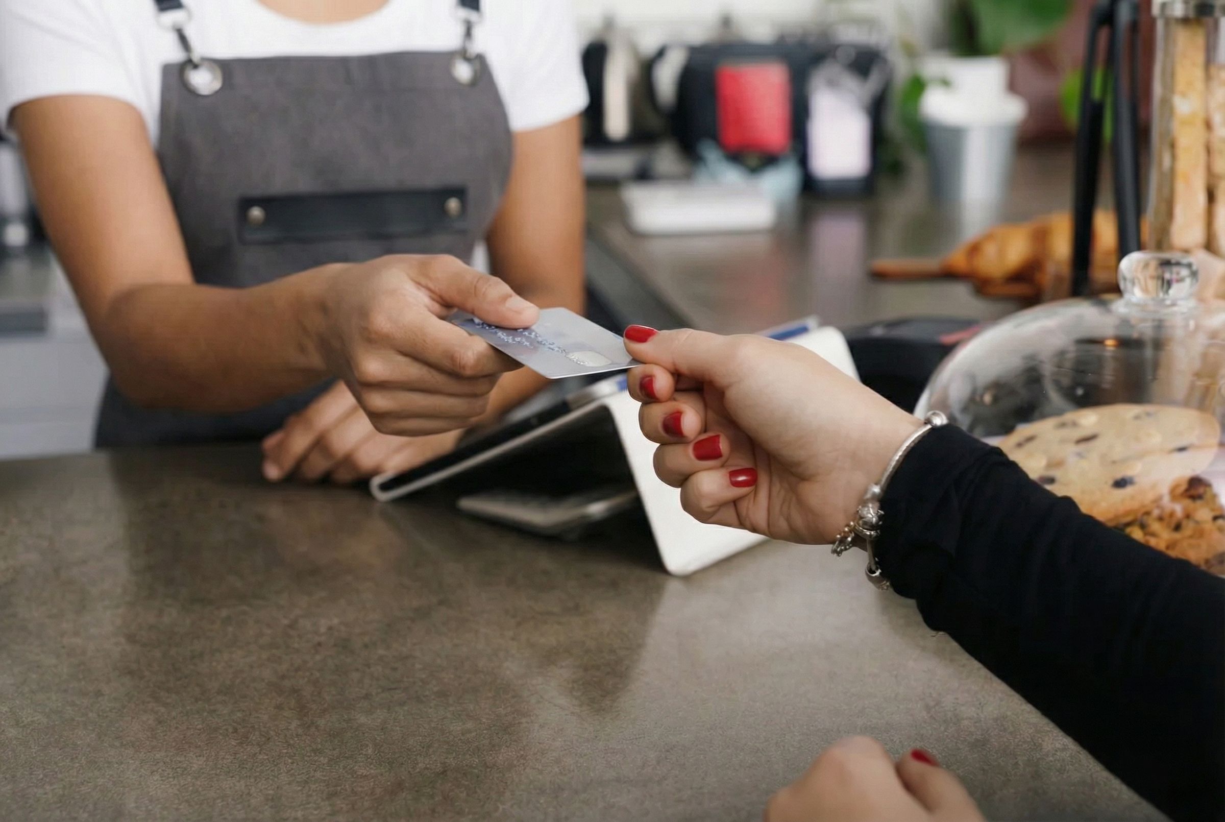 Barista in apron takes a customer’s credit card over a café counter with pastries displayed
