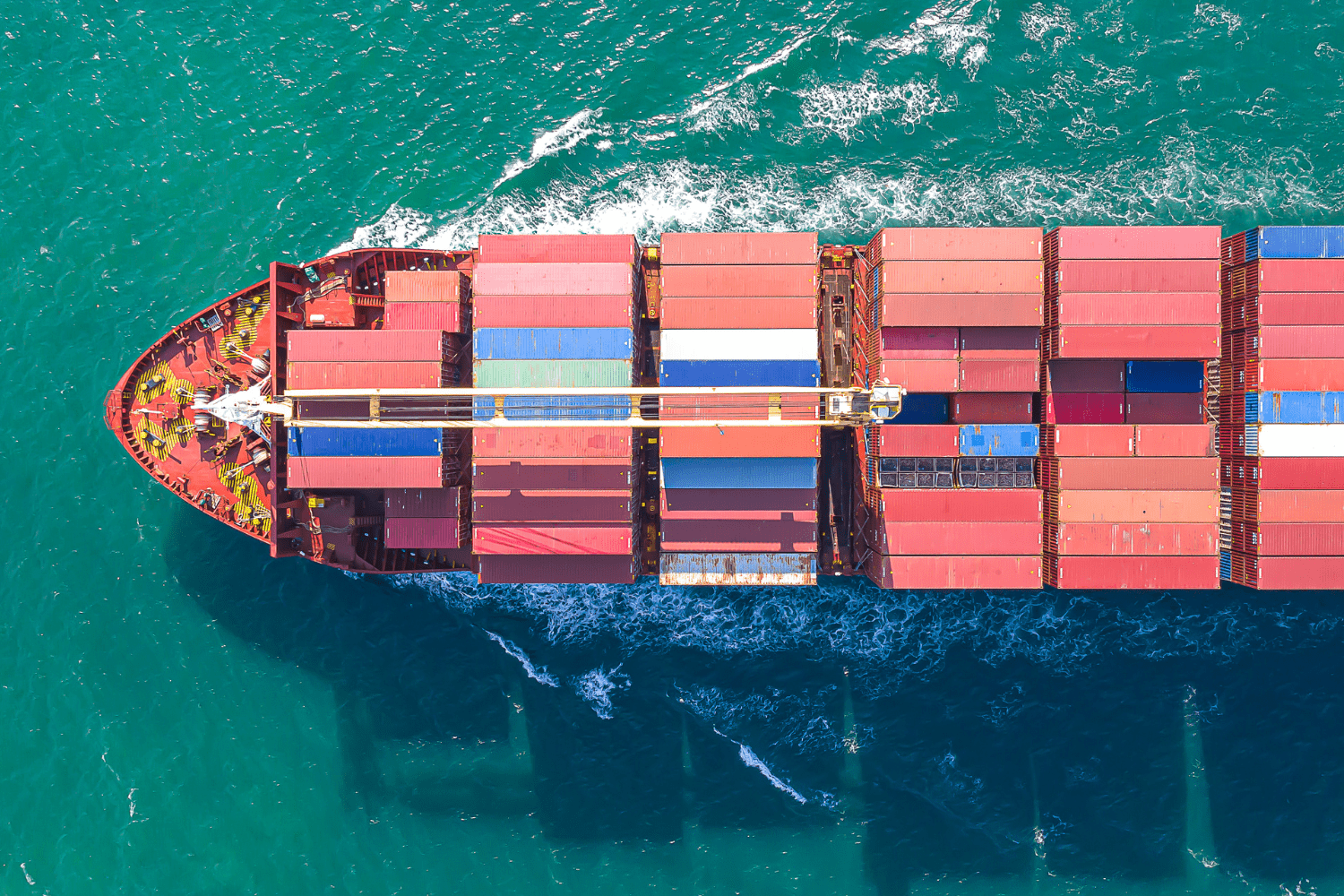 Aerial view of a cargo ship loaded with colorful containers sailing through turquoise water