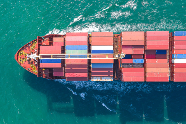 Aerial view of a cargo ship loaded with colorful containers sailing through turquoise water