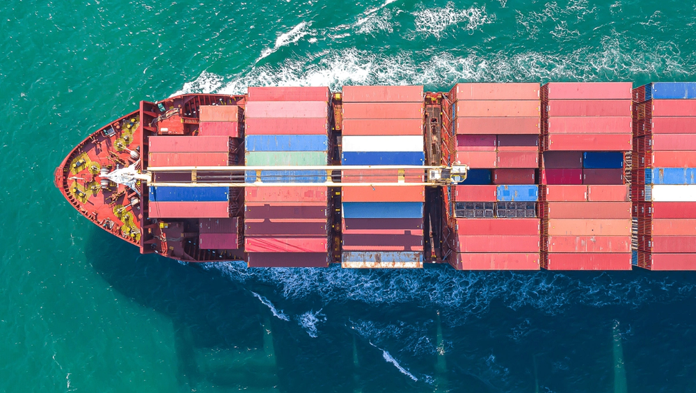Aerial view of a cargo ship loaded with colorful containers sailing through turquoise water