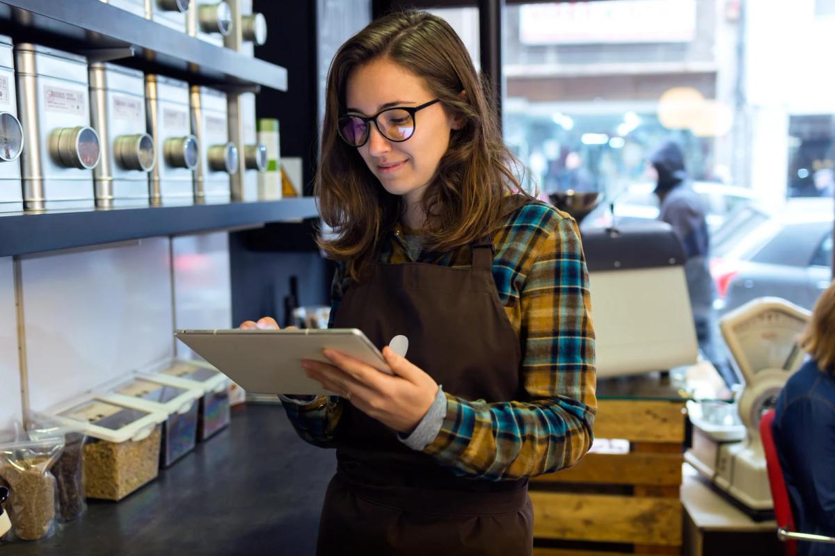 Barista in apron using a tablet behind the counter of a modern coffee shop