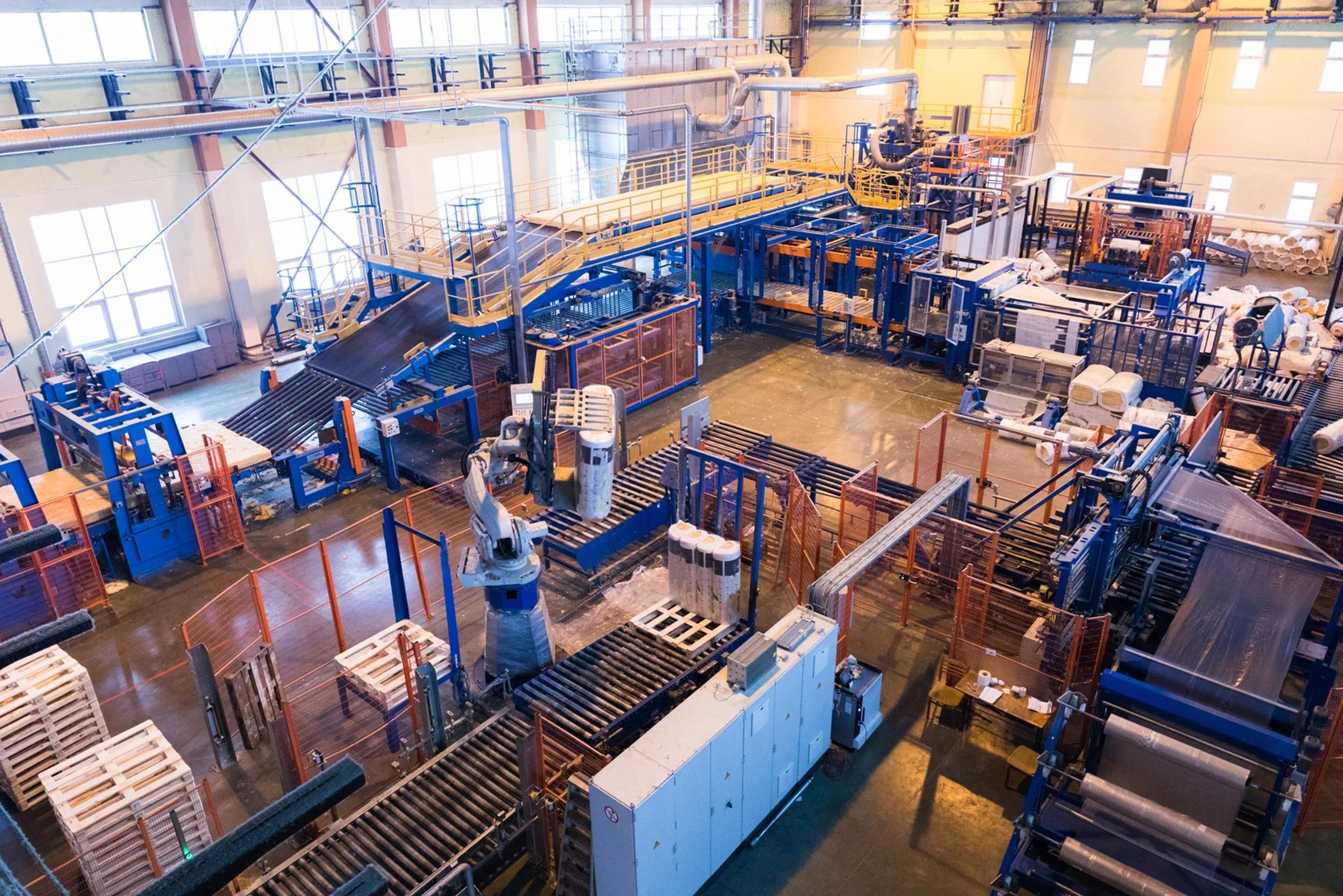 Automated factory floor with conveyor belts, robotic arms, machinery, and stacked materials.