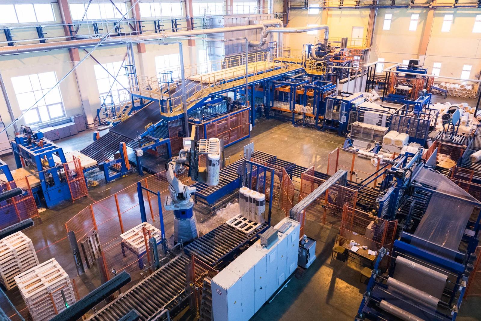 Automated factory floor with conveyor belts, robotic arms, machinery, and stacked materials.