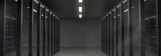 Long hallway of dark server racks in a data center with overhead fluorescent lighting