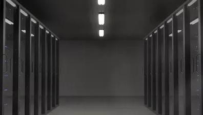 Long hallway of dark server racks in a data center with overhead fluorescent lighting