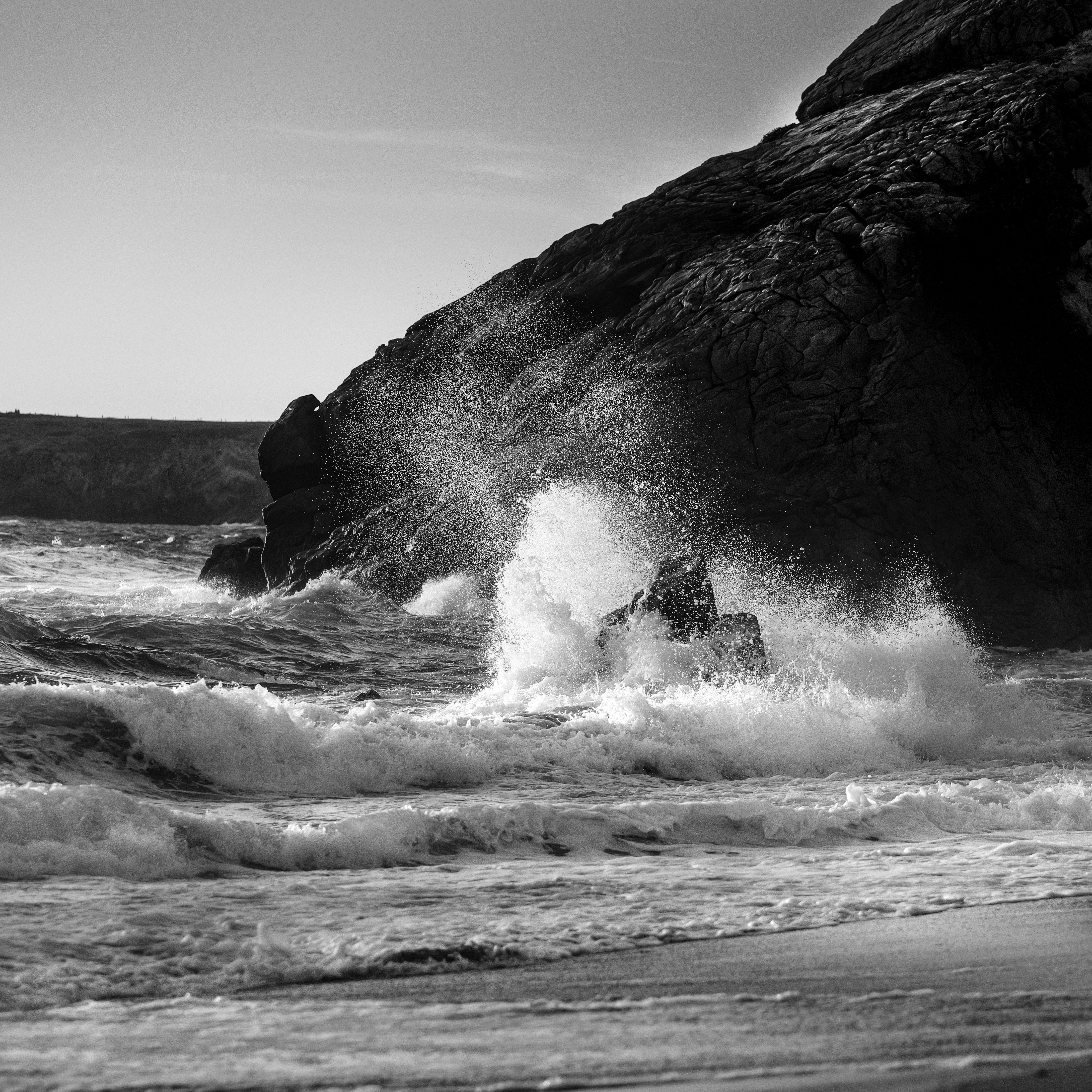 Black-and-white seascape of a wave exploding against a dark coastal rock at Plage de Bara, Quiberon.