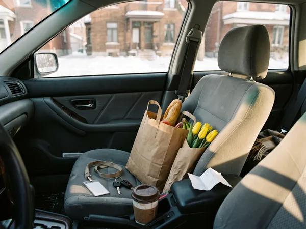 A work ID lanyard, car keys, groceries and yellow tulips on a car passenger seat, on the way to help a parent.