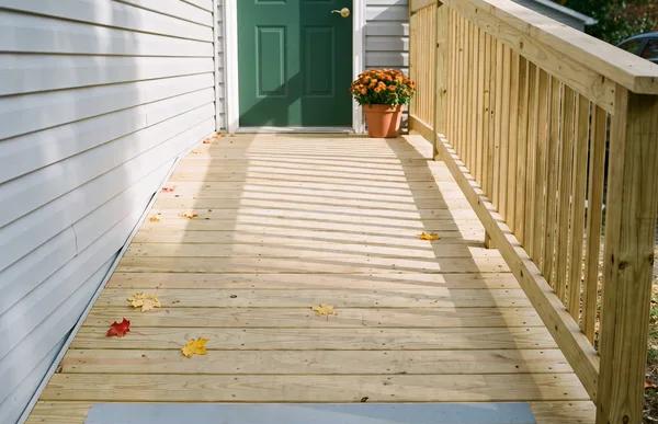 A newly built wooden access ramp with railings and an anti-slip strip runs up to a green side door in autumn sun