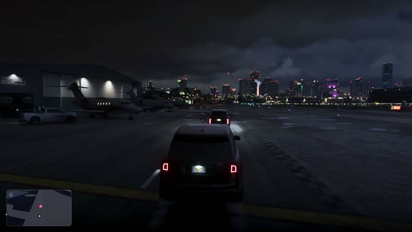 Gameplay of an SUV following another across an airfield at night, with private jets by a hangar and the Vice City skyline behind.