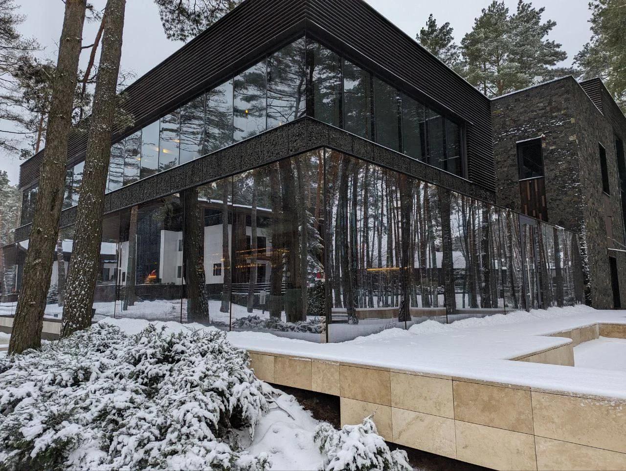 Modern custom home among mature trees with dark cladding, large windows, and snow-covered terraces