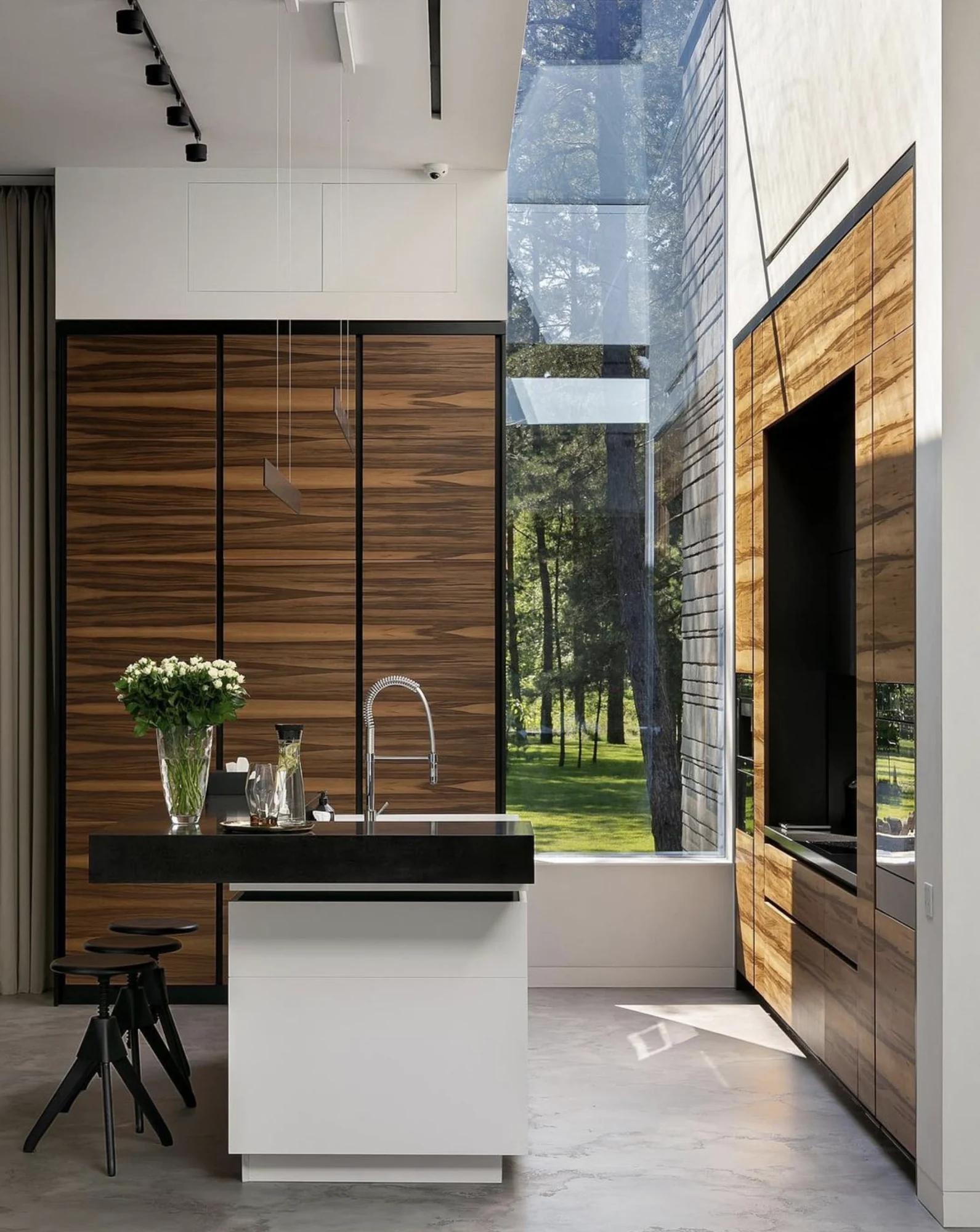 Completed custom kitchen with book-matched wood cabinetry, black island, and full-height garden glazing