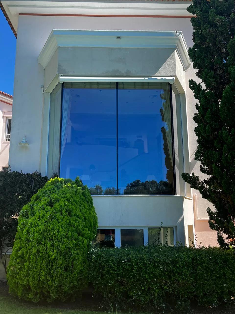 Large floor-to-ceiling residential picture window with blue sky and garden reflections