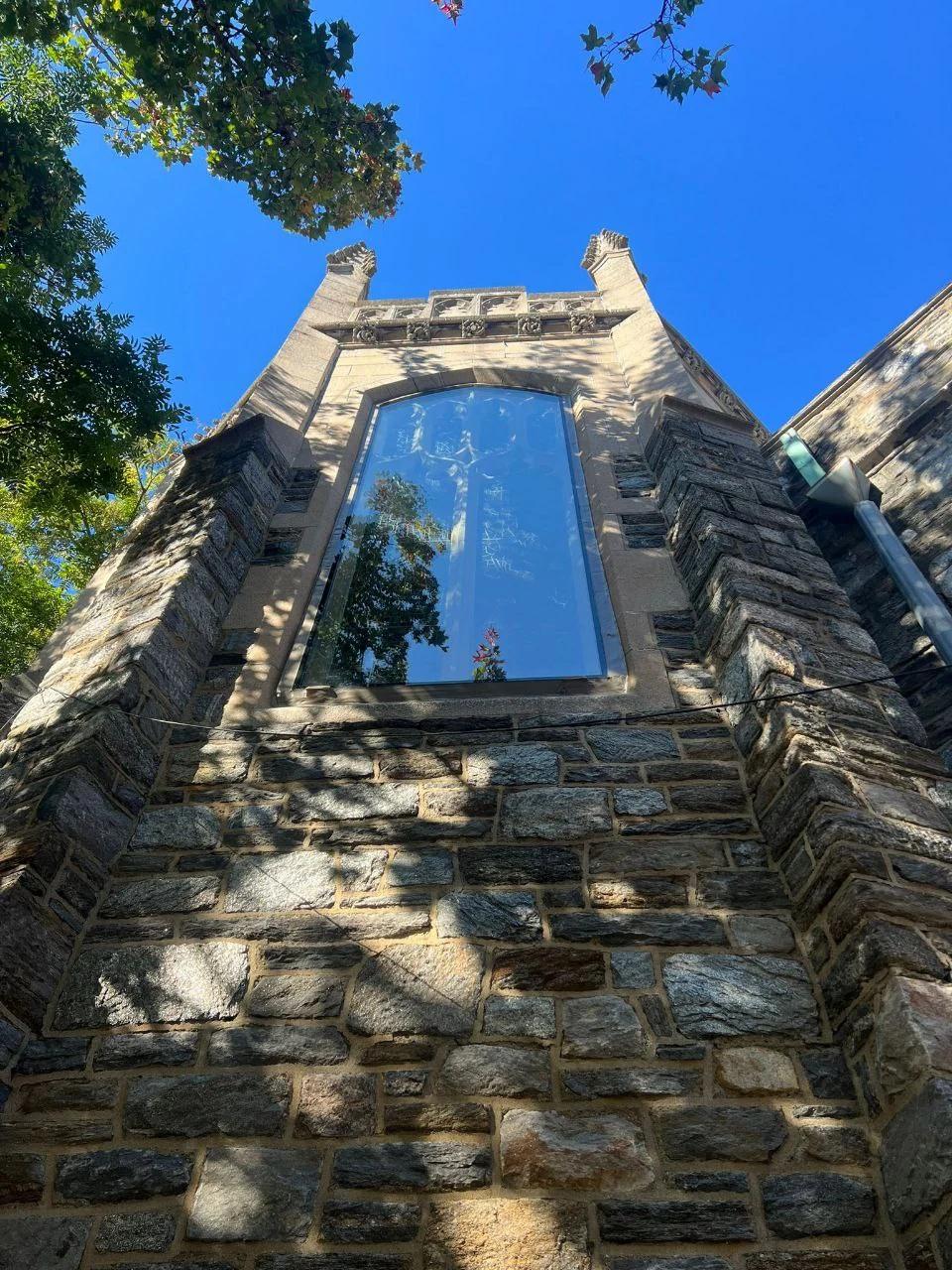 Tall custom residential window installed within a natural stone facade