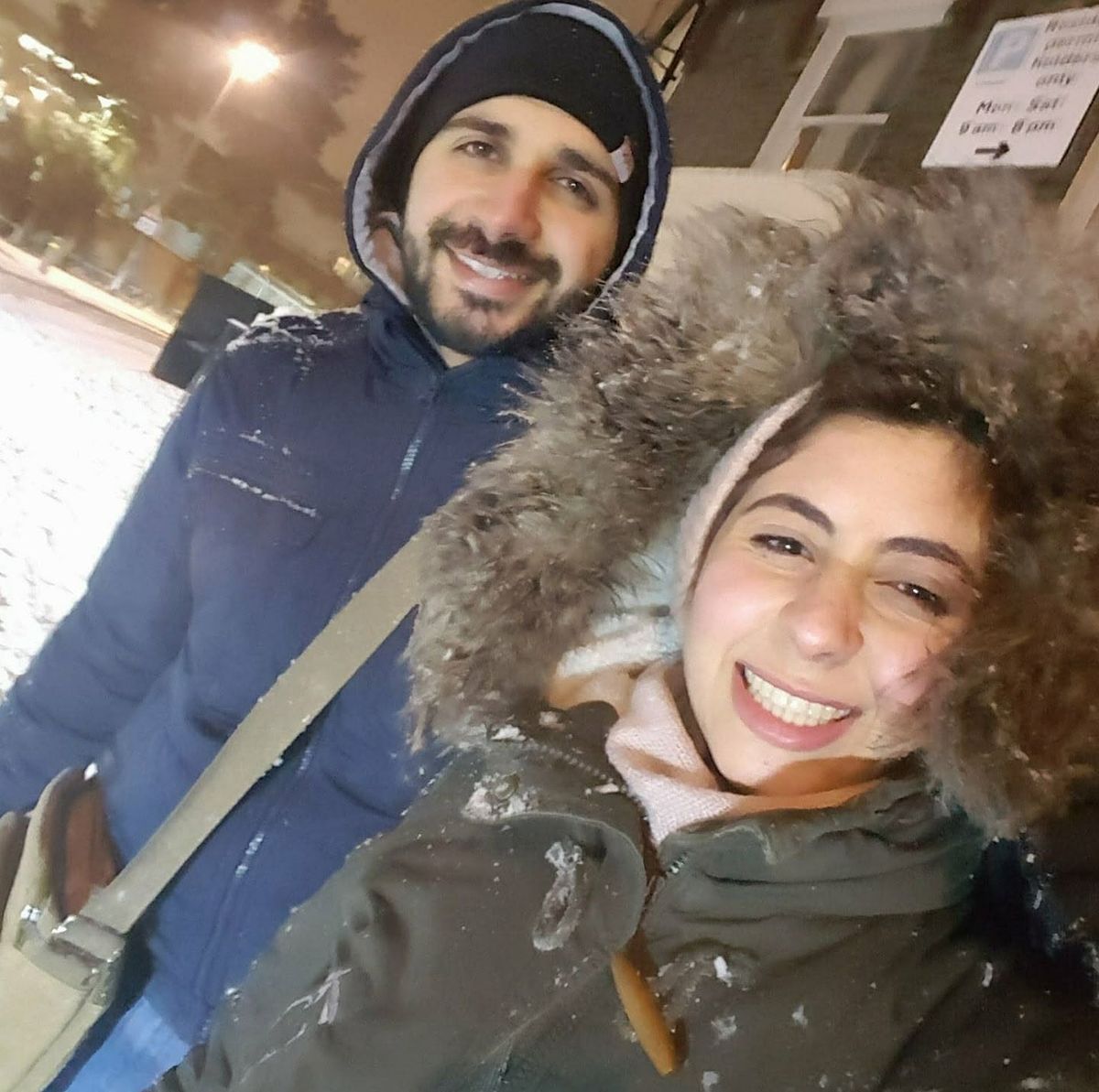 Maged and his wife smiling for a selfie outdoors on a snowy night, bundled up in winter coats.