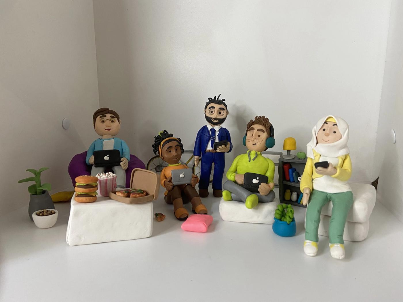 Five handmade clay characters with laptops, tablets and phones, surrounded by tiny food, plants, cushions, a bookshelf and a bicycle.