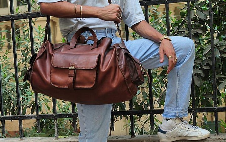 A seated person holding a brown leather bag outdoors.