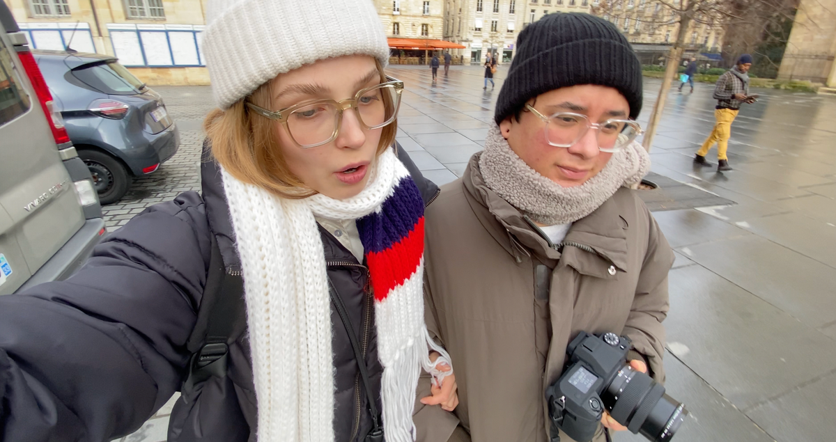 two people standing next to each other with one holding a canon camera