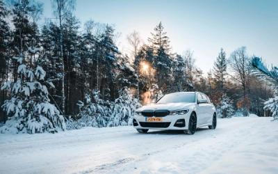 a white car is parked on a snowy road in the woods .