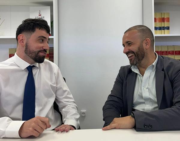 two men are sitting at a table in front of a sign that says apex