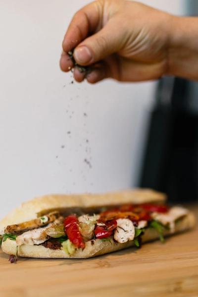 a person is sprinkling pepper on a sandwich on a cutting board .