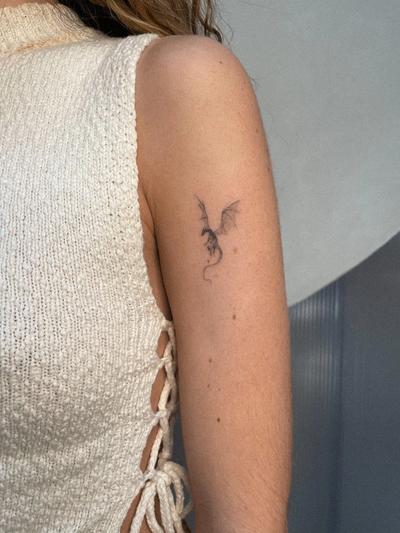 una mujer tiene un pequeño tatuaje de un dragón en el brazo .
